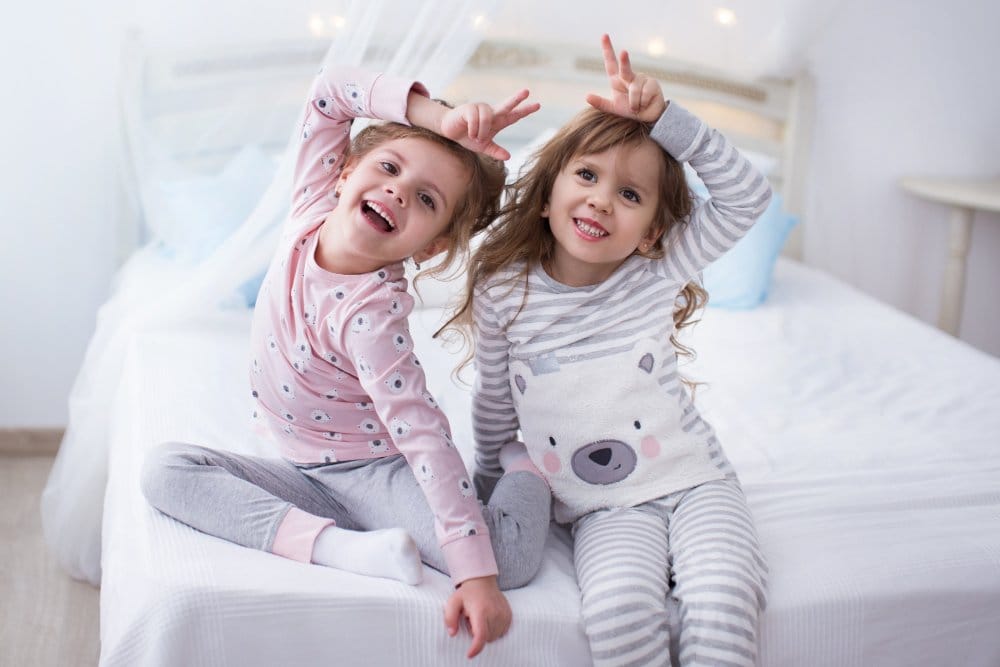 Two little girls wearing pajamas sitting on the bed and posing for a photo