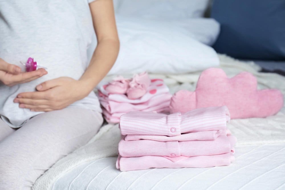 Pile of baby sleepers and pregnant woman on bed
