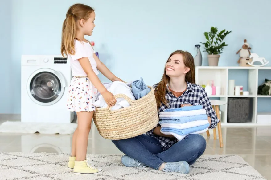 Mother and young daughter folding clean laundry together at home
