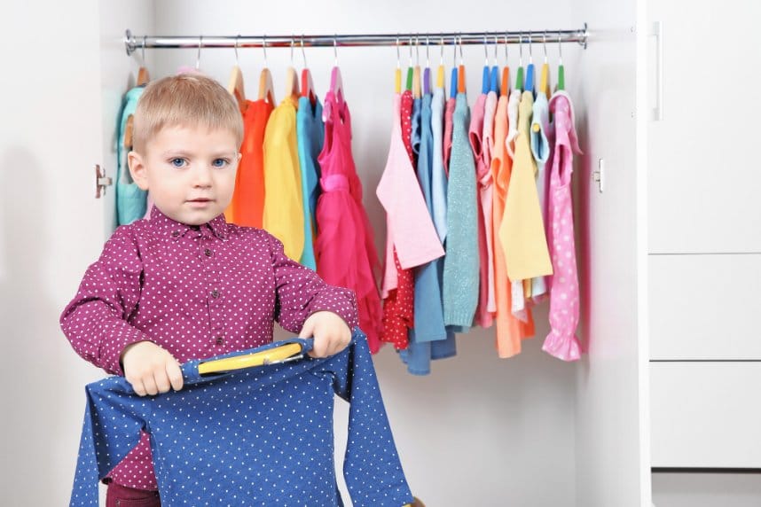 Young boy choosing shirt from organized toddler wardrobe
