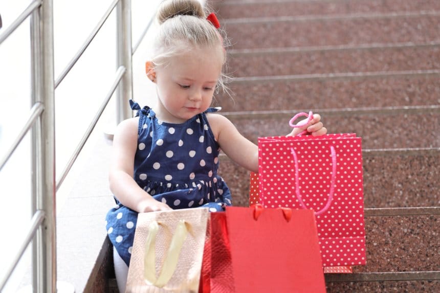 Little girl sitting with colorful shopping bags after clothing purchase