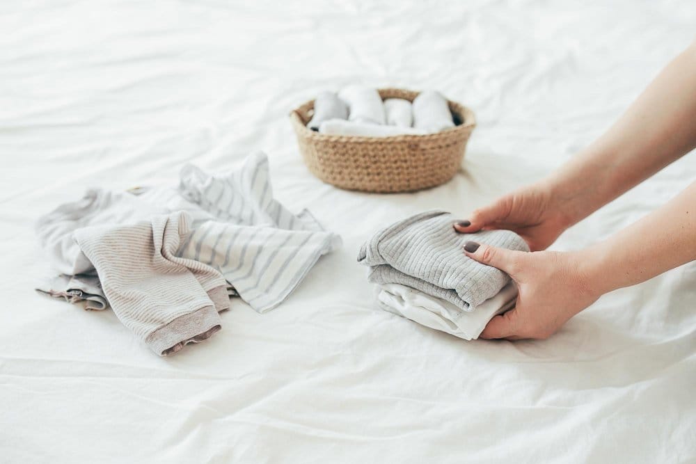 A woman folding various baby clothes in different fabric