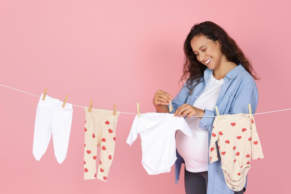 A pregnant woman air-drying baby clothes on a line dryer