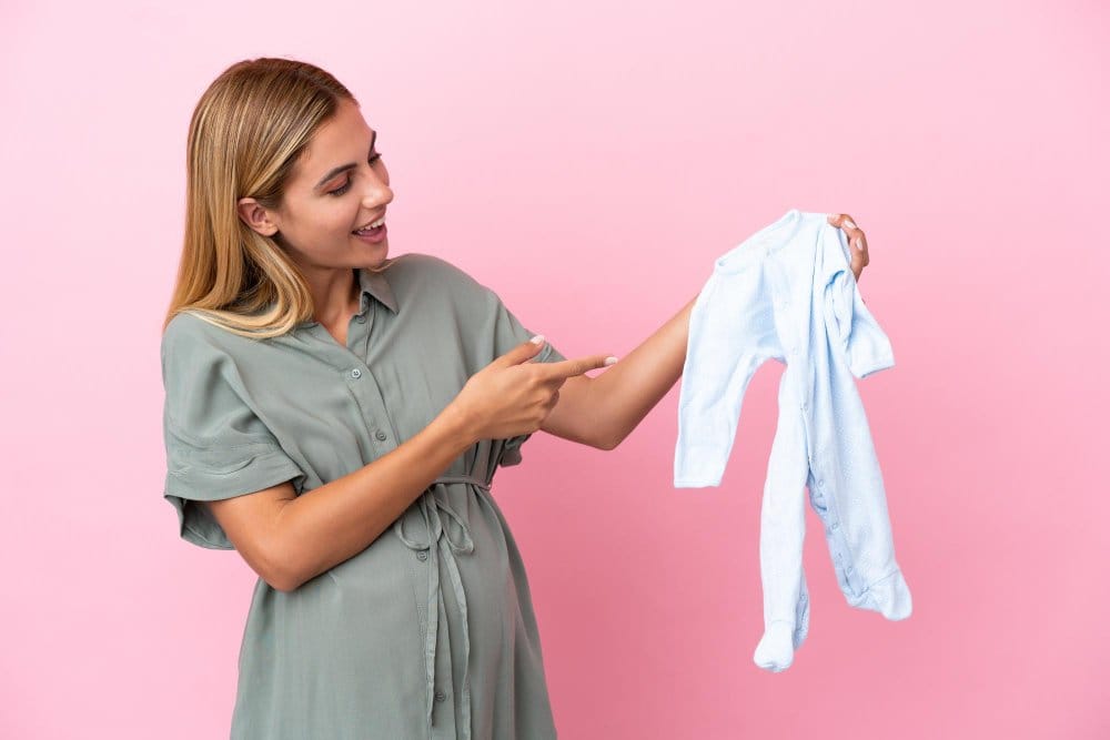 A pregnant woman holding a baby bodysuit