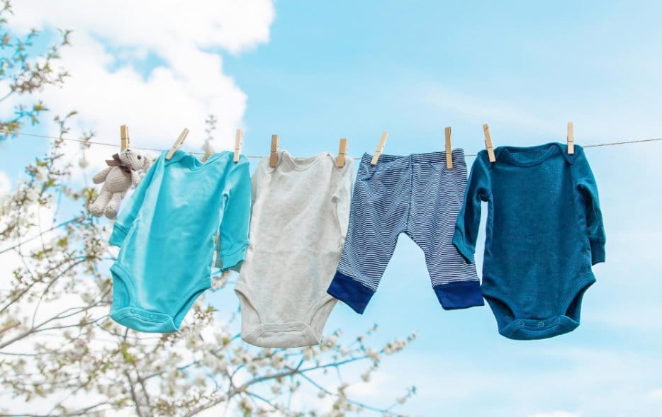 Baby clothes hung on clothing line outside while the sun is shinning