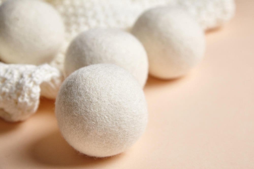 Closeup of wool dryer balls placed beside a textured white knitted fabric on a soft beige background