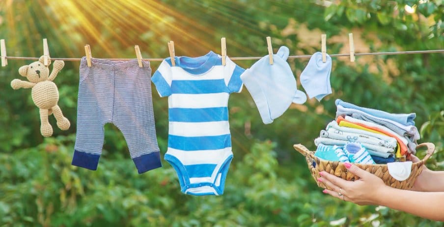 Baby clothes hung on a clothing line outside and a woman's hand carrying a basket full of folded laundry
