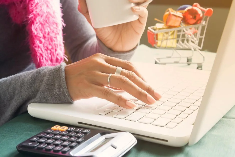 Woman sipping tea while calculating various costs and expenses on laptop and calculator