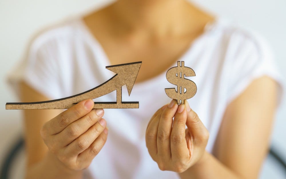 Closeup of woman's hand holding wooden dollar sign and line and arrow sign demonstrating profitability