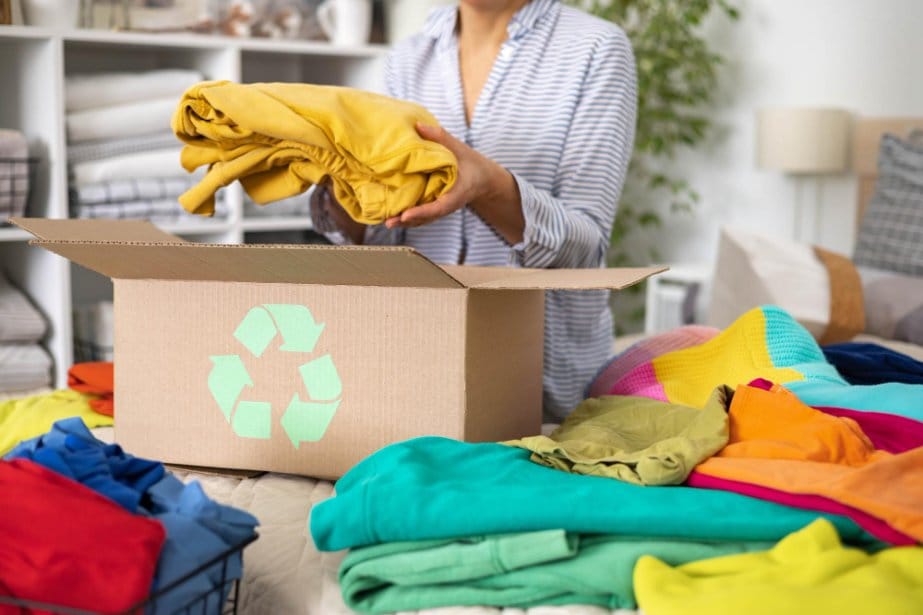 The concept of recycling clothes a woman puts bright colored clothes in a box with a recycle sign