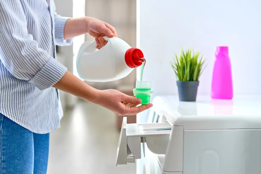 Person pouring liquid laundry detergent into washing machine drawer