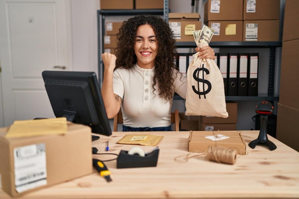 Happy online seller in a small stock room holding a money bag after making successful sales on Vinted