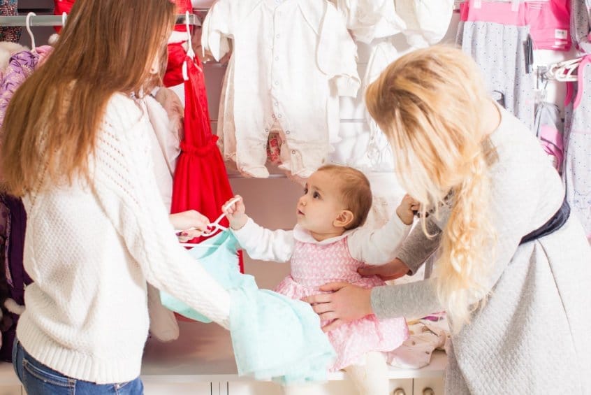 Two women helping toddler try on new outfit in clothing store