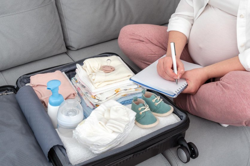 A pregnant woman packing toddler clothes in suitcase and using a checklist