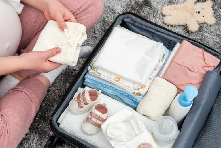 Pregnant woman sitting on the floor packing toddler clothes for travel