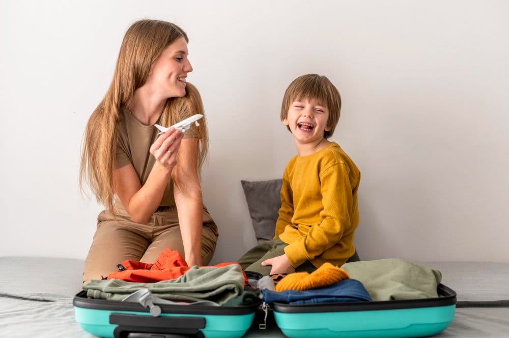Mother and son having fun packing clothes in suitcase and playing with a toy