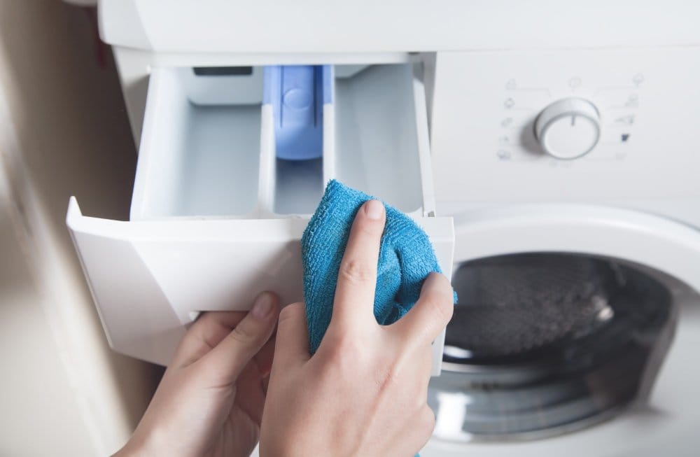 Person cleaning washing machine detergent drawer with cloth