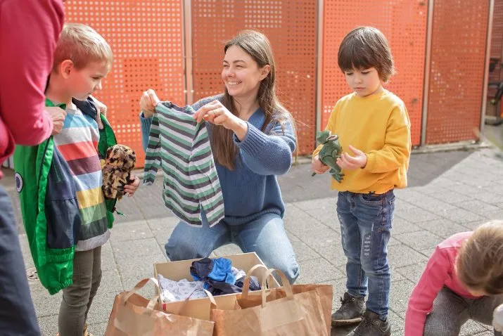 Two parents exchanging a box of toddler clothes in a friendly hand-me-down exchange