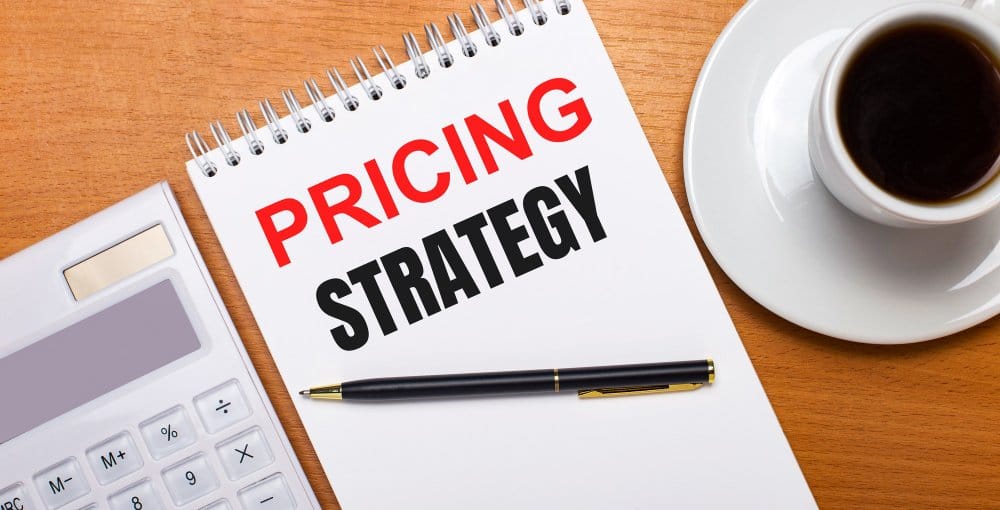 Notebook labeled pricing strategy beside calculator and coffee cup