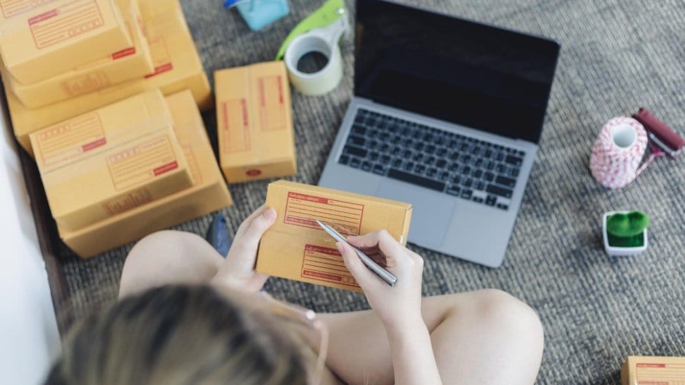 Person labeling small parcels near laptop for shipping sold clothes