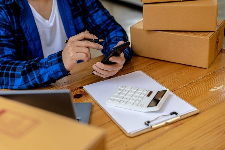 Seller calculating expenses with boxes and calculator for resale taxes