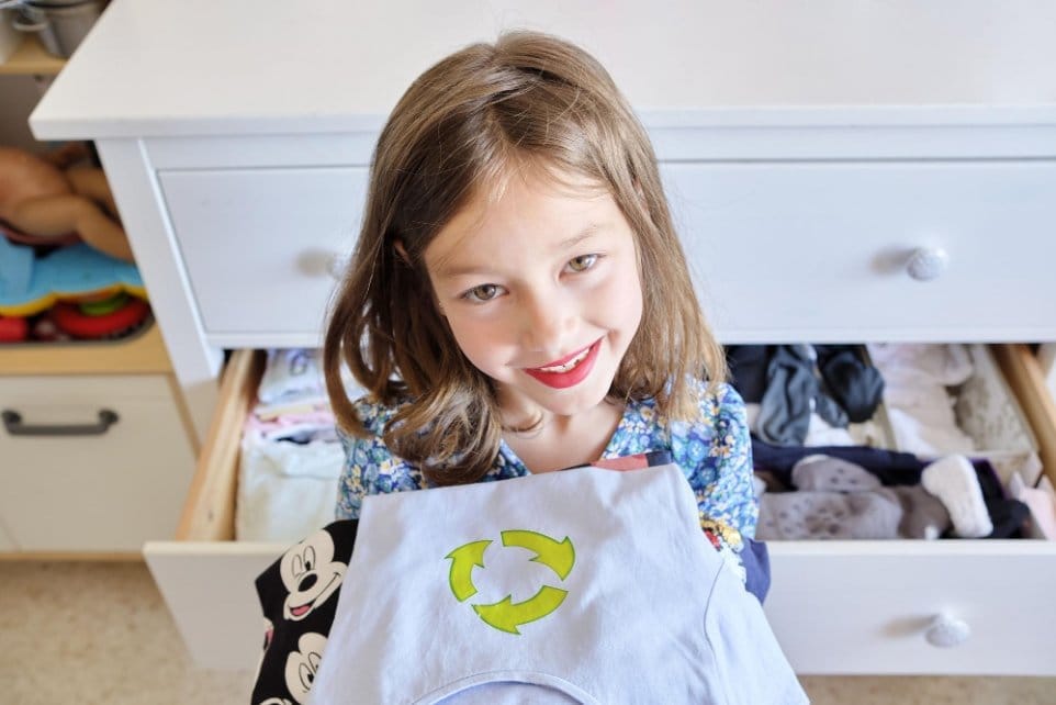Smiling child holding shirt with recycle symbol, promoting sustainable fashion