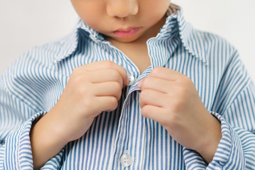 Little boy attempting to button up his shirt