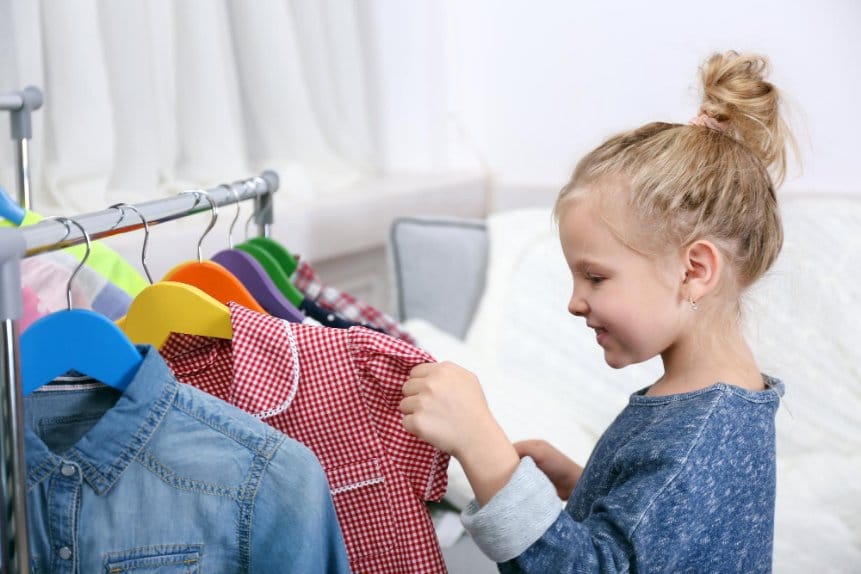 Little girl going through various clothes on a rack
