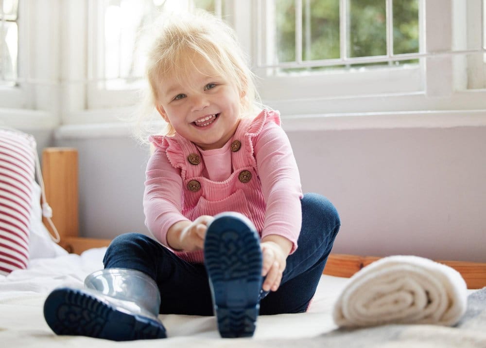 Smiling little girl sitting on the floor attempting to wear her boot