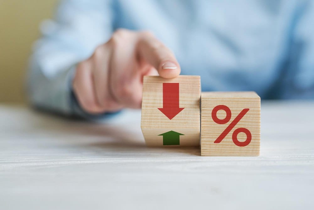 Close-up of a person's hand flipping a wooden block with red downward and green upward arrows next to another wooden block displaying a red percentage symbol, representing changes in percentages on listings on eBay or vonted