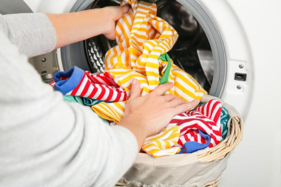 Placing colorful toddler clothes into washing machine drum