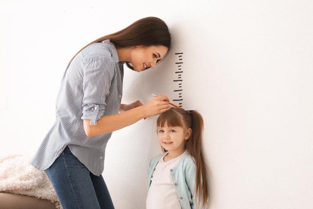 Mother measuring young girl's height against wall chart