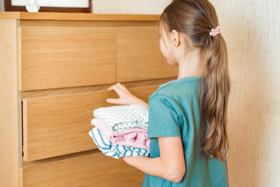 Happy little girl puts old clothes in order for storage
