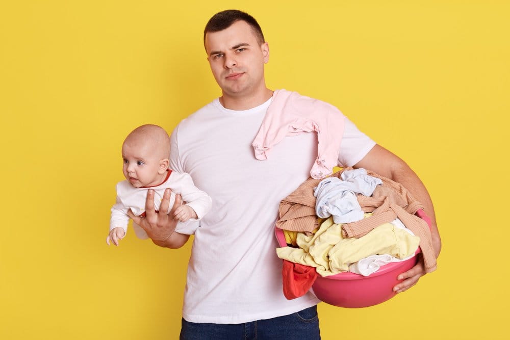 A man carrying a baby on one hand and laundry on the other hand