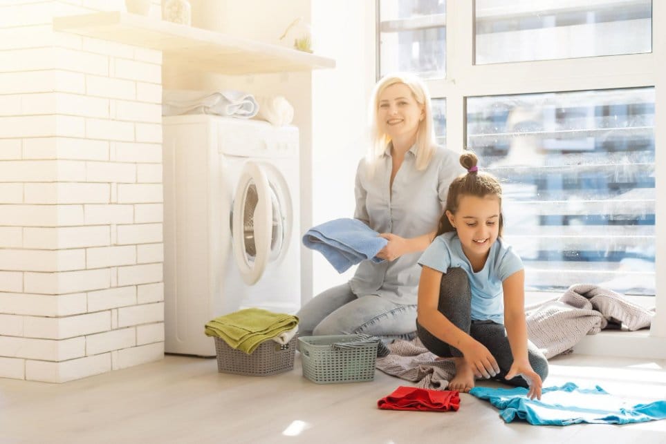 Mom and little daughter doing laundry together near washing machine