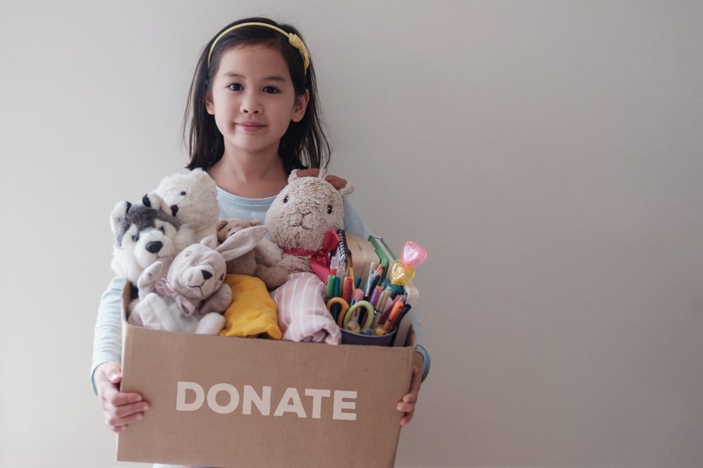 Young volunteer girl holding a box full of used toys, cloths, books and stationery for donation