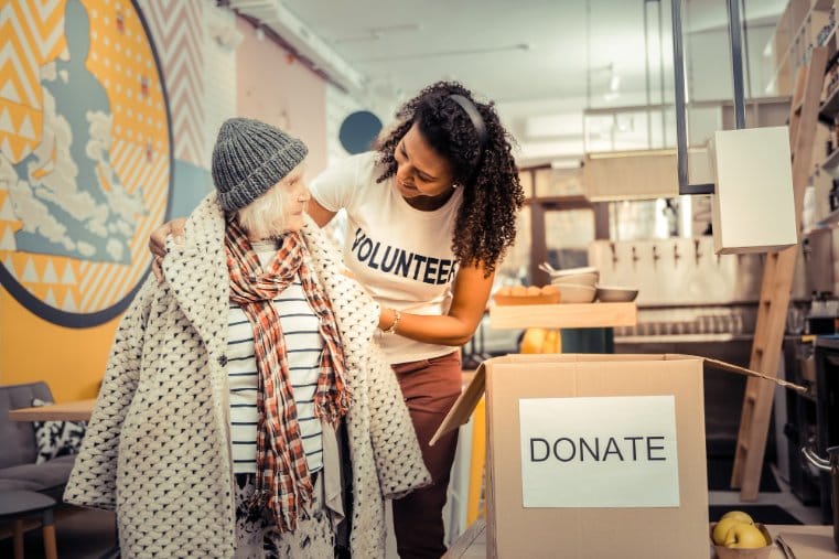 Friendly woman smiling while helping a woman in need to wear a coat