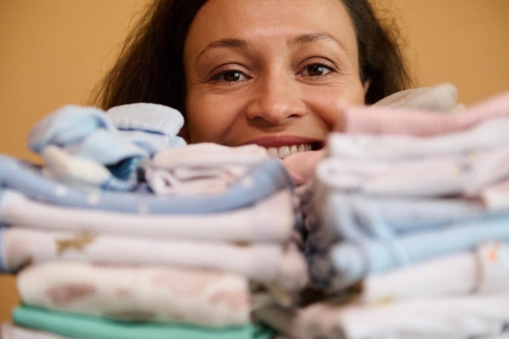 Smiling woman behind a pile toddler clothing