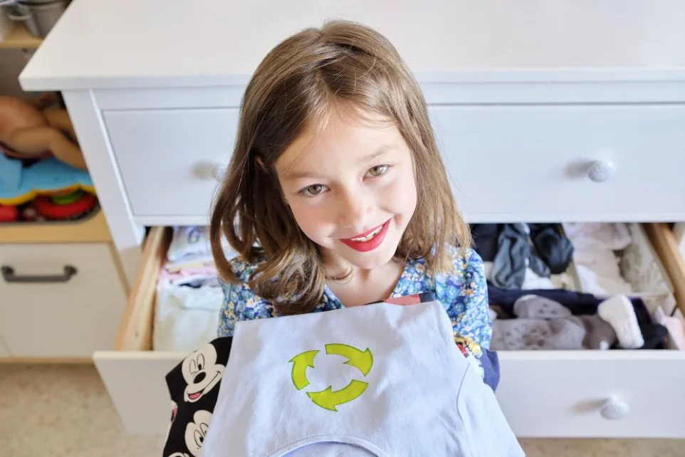 Little girl in a blue dress happily organizing her clothes for donation and reusing