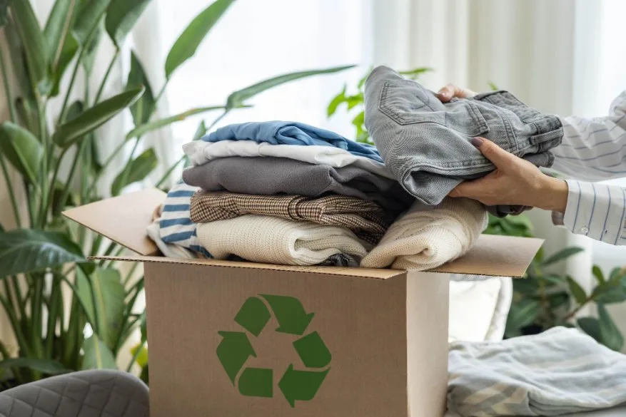 A woman at home collects clothes in a box for recycling