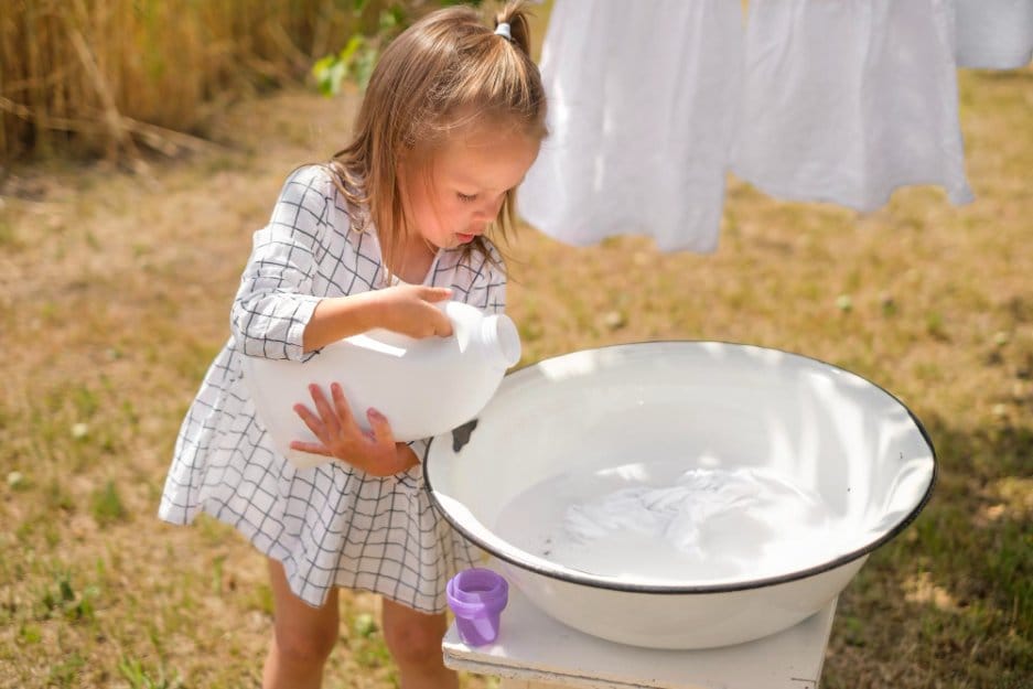 Little girl pours laundry detergent into a washbasin