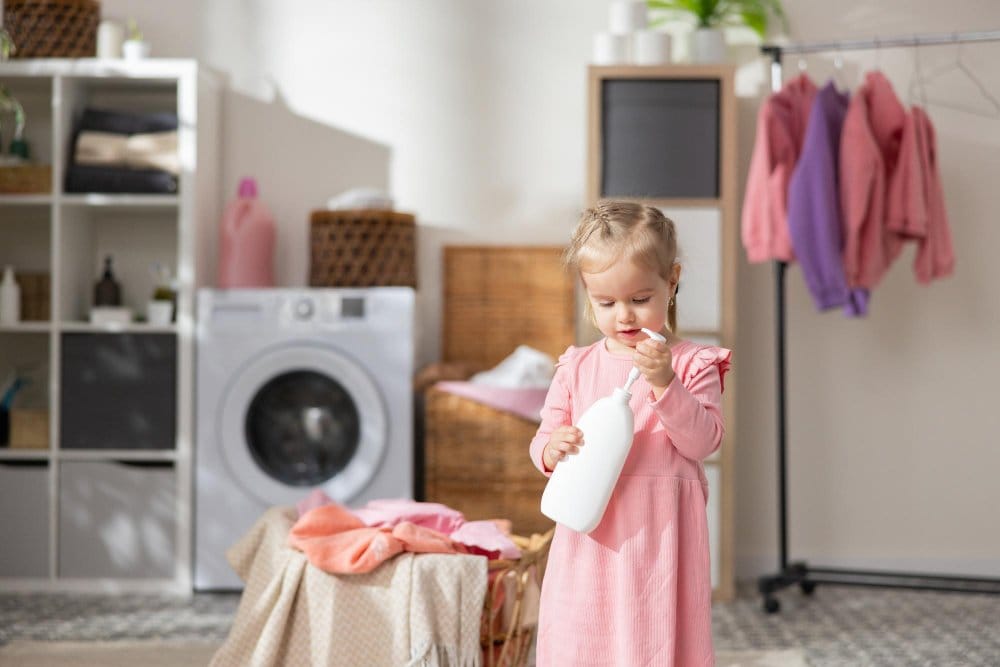 A little girl holding a stain remover container in the laundry