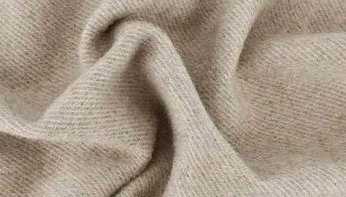 Close up of soft beige acrylic fabric with visible knit texture and cozy wool like appearance