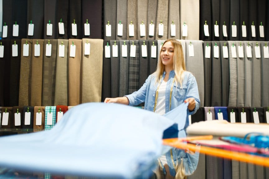 Woman examining blue fabric roll in textile store to check quality and texture