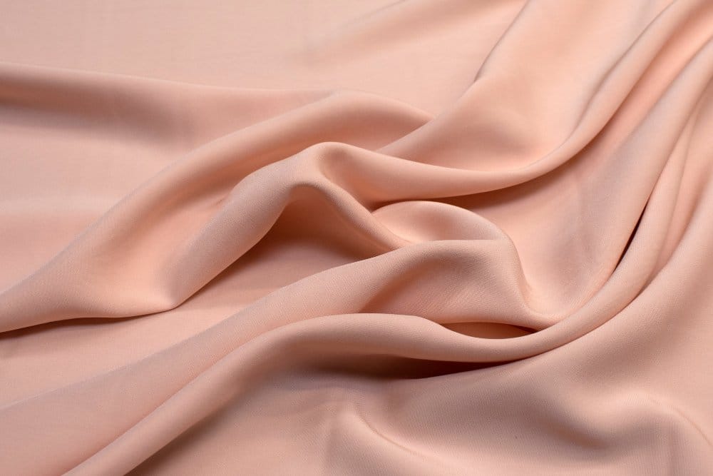Peach colored semi synthetic fabric with soft drape and smooth surface texture