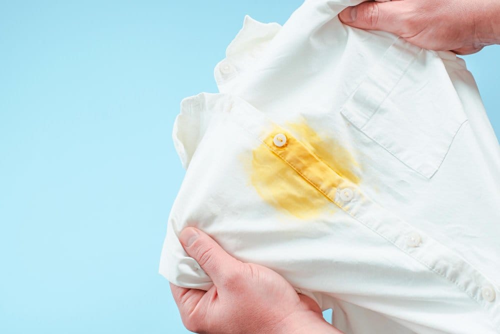 White shirt with yellow stain being held for stain removal demonstration