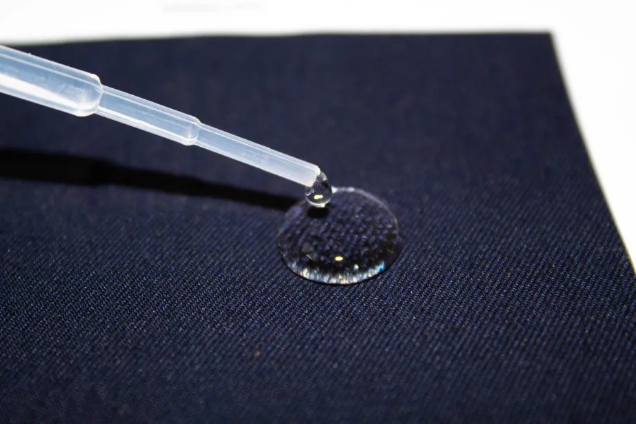 Dropper placing water on dark fabric to evaluate water repellency performance
