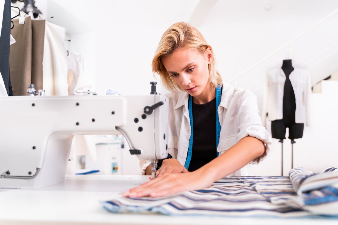 seamstress using sewing machine while working with striped fabric during garment construction