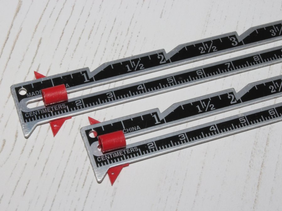 Two metal seam gauges with red sliders used for sewing measurements.
