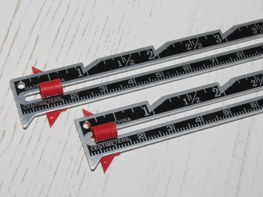 Two metal seam gauges with red sliders used for sewing measurements.